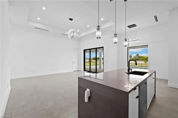 Kitchen with hanging light fixtures, an island with sink, a tray ceiling, sink, and plenty of natural light