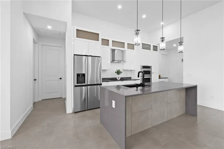 Kitchen featuring stainless steel appliances, hanging light fixtures, a kitchen island with sink, white cabinetry, and wall chimney exhaust hood