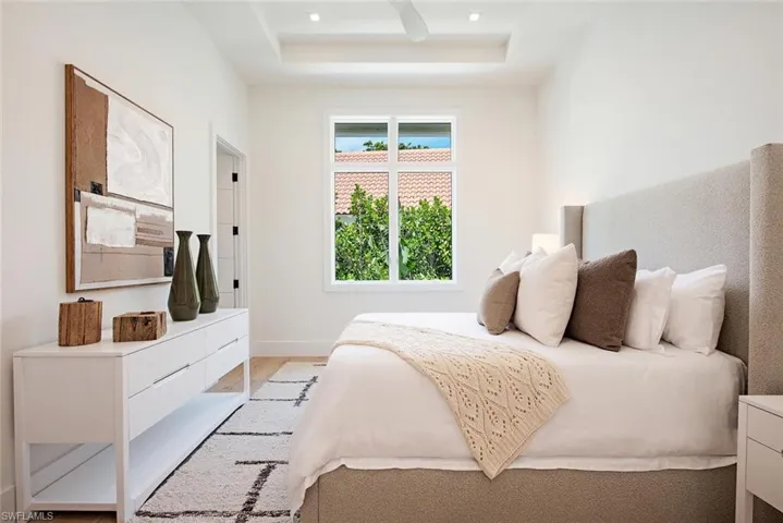 Bedroom featuring baseboards, light wood finished floors, and a raised ceiling