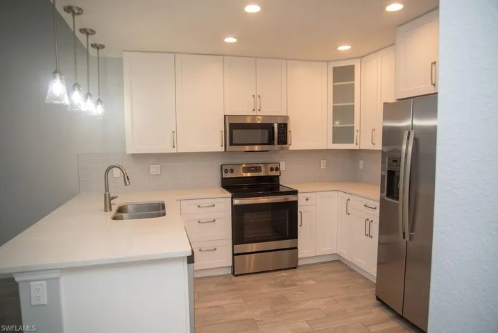 Kitchen with white cabinetry, stainless steel appliances, light hardwood / wood-style floors, and sink