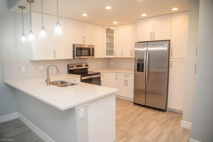 Kitchen featuring white cabinetry, sink, hanging light fixtures, kitchen peninsula, and stainless steel appliances