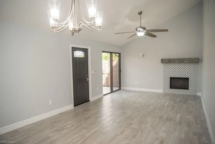 Unfurnished living room with a tile fireplace, vaulted ceiling, ceiling fan, and light wood-type flooring