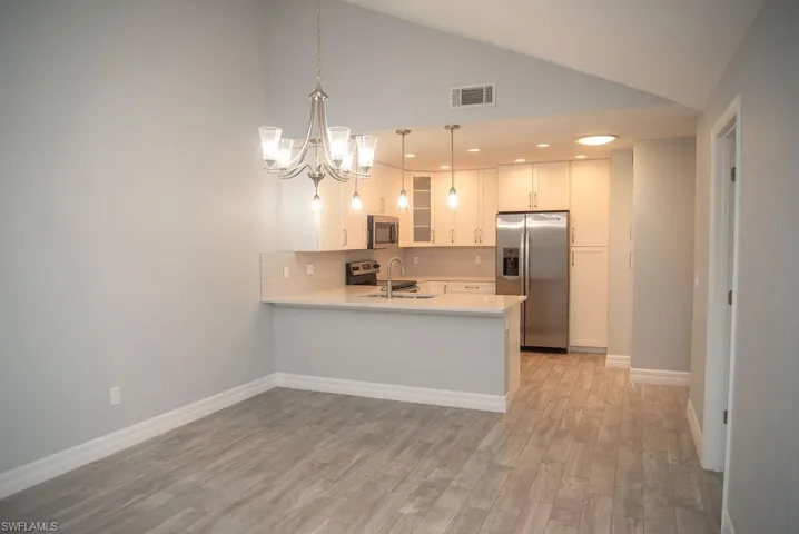 Kitchen with white cabinetry, decorative light fixtures, light wood-type flooring, kitchen peninsula, and stainless steel appliances