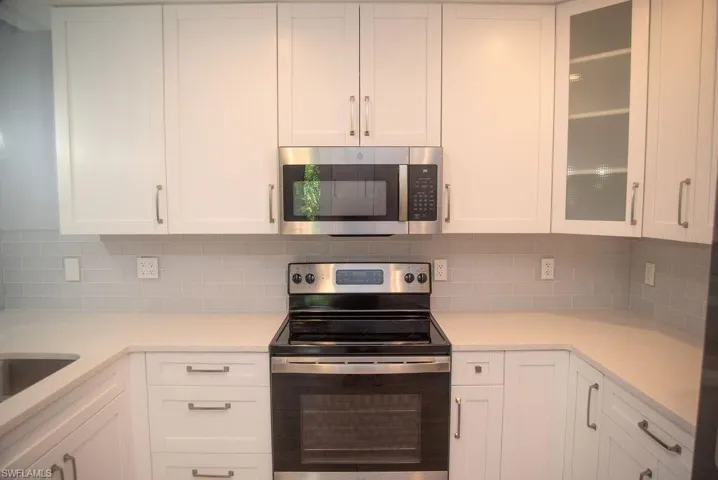 Kitchen with backsplash, appliances with stainless steel finishes, and white cabinets