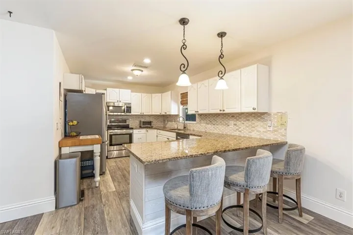 Kitchen featuring light stone counters, pendant lighting, a peninsula, appliances with stainless steel finishes, and white cabinets