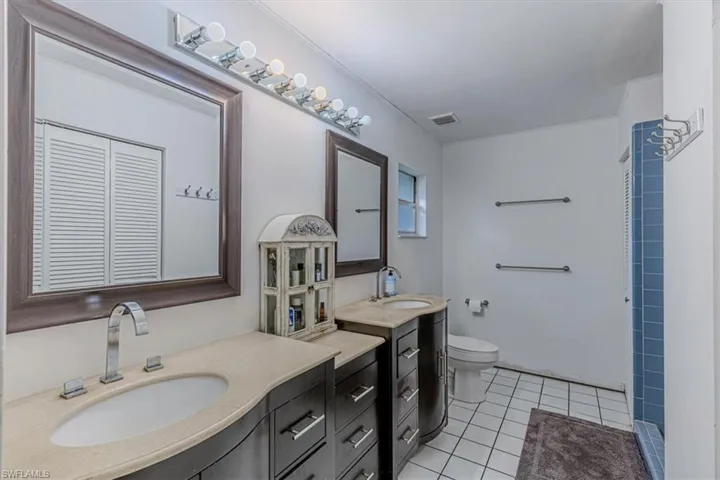 Bathroom with light tile patterned flooring, two vanities, and a shower