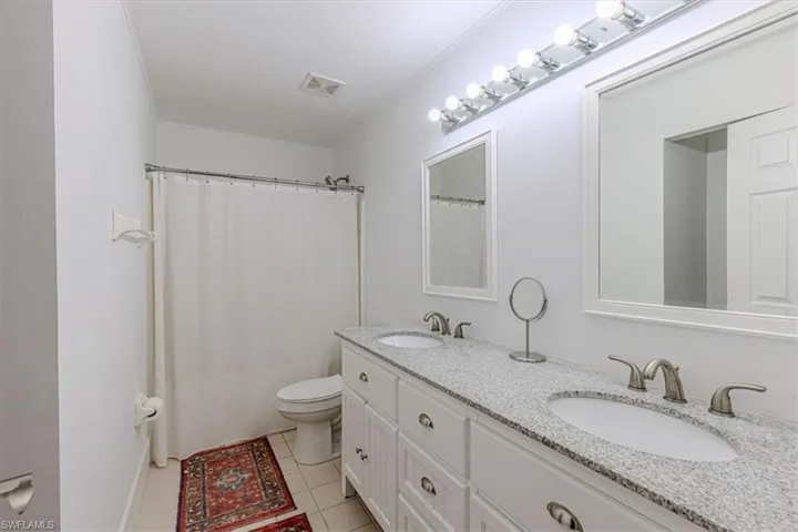 Full bathroom with a shower with shower curtain, double vanity, and light tile patterned floors