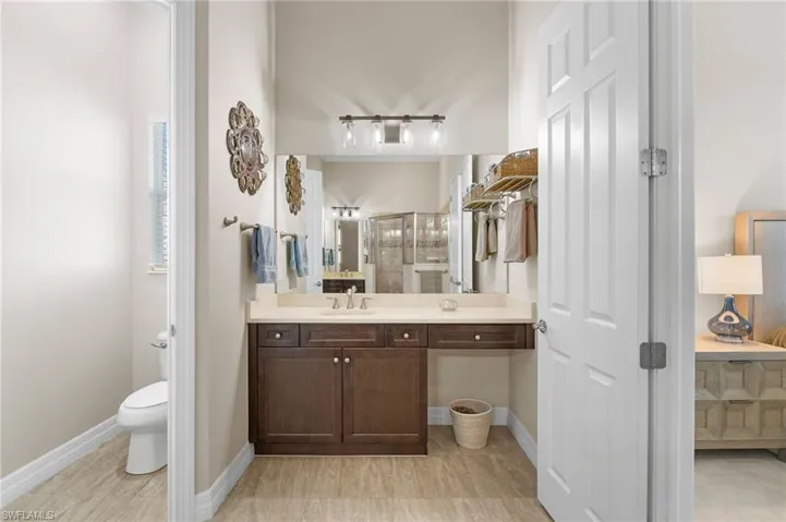 Bathroom featuring a dark wood cabinetry vanity with a stone-top counter, undermount sink, expansive wall mirror, and three-light vanity fixture