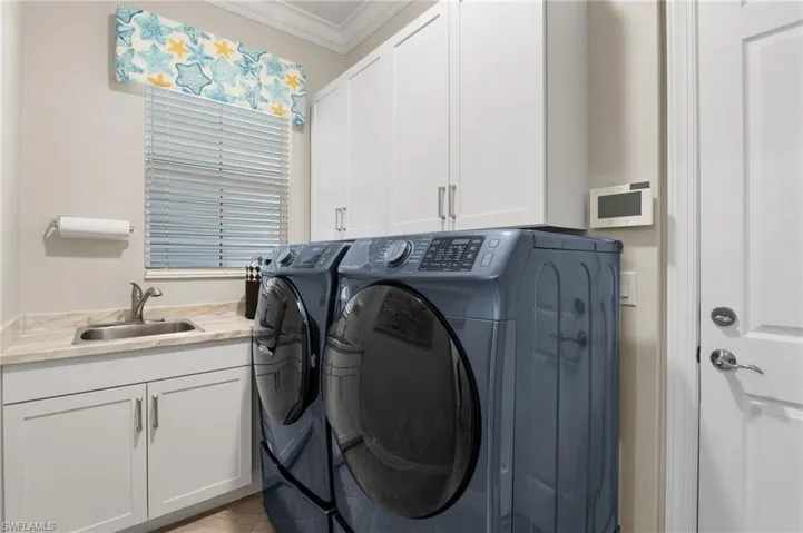 Laundry room featuring white Shaker-style cabinetry, a light-toned laminate countertop, an integrated stainless steel sink with a high-arch faucet, and crown molding