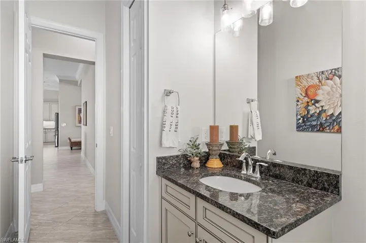 Bathroom vanity featuring stone-finish countertop, undermount sink, shaker-style cabinetry, and wall-mounted light fixture with frosted glass shades