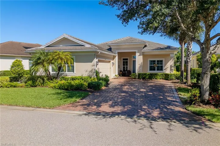 Single-story residence featuring a paved brick driveway, multi-gabled roofline, stucco exterior, covered entryway, and landscaped grounds