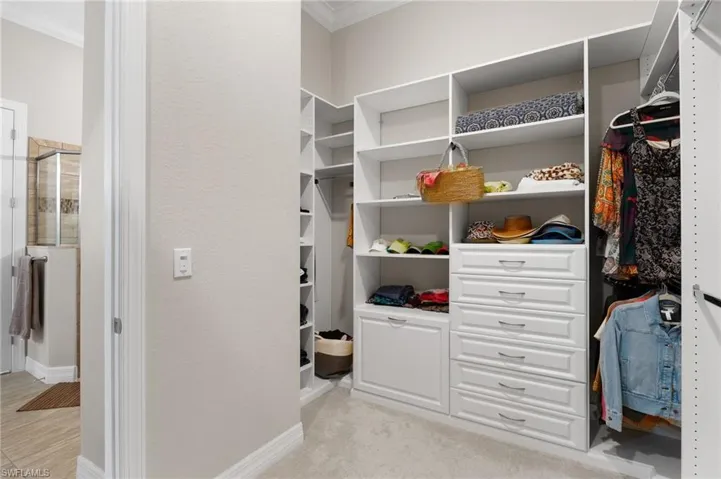 Walk-in closet featuring white custom built-in shelving, floor-to-ceiling storage units, multiple tiered hanging rods, and a stack of six integrated soft-close drawers with brushed nickel hardware