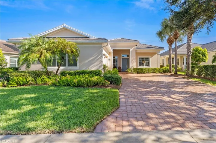 Single-story residence featuring a paved brick driveway, stucco exterior, hip roof, and manicured landscaping with mature palms