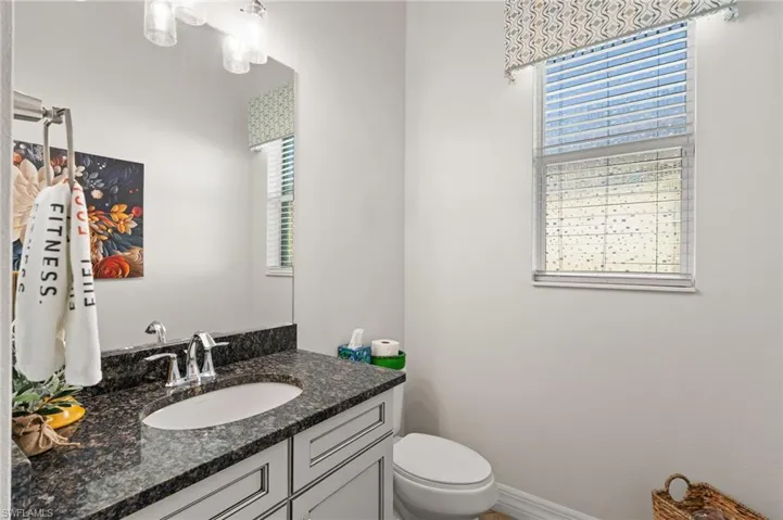 Stone countertop featuring an integrated undermount sink, shaker-style cabinetry, chrome faucet, and expansive wall-mounted mirror