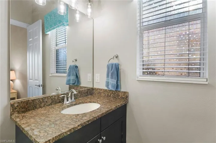 Vanity with stone-finish countertop, undermount sink, dual-handle polished metal faucet, dark wood-finish cabinetry, and full-width wall mirror