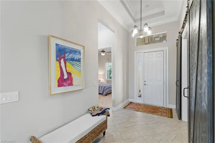 Entryway featuring a tray ceiling, tile flooring, multi-panel entry door with a transom window, and a rustic wood sliding barn door