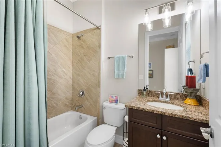 Full bathroom featuring a dark wood-finish vanity, stone-patterned countertop with an undermount sink, porcelain tile tub surround in a diagonal pattern, and a three-light wall-mounted fixture