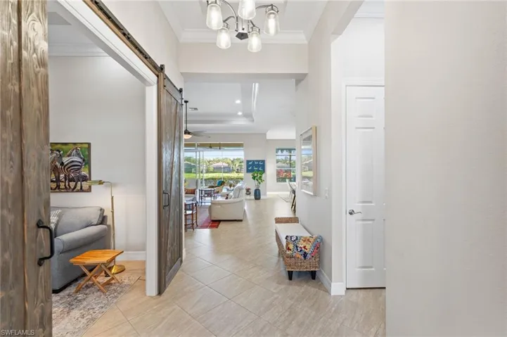 Entryway featuring wood-finish barn doors, crown molding, multi-light chandelier, and large-format tile flooring
