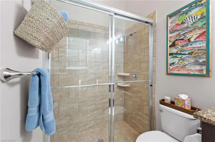 Walk-in shower featuring a sliding glass enclosure, floor-to-ceiling tile surround, built-in shelving, and a chrome shower head