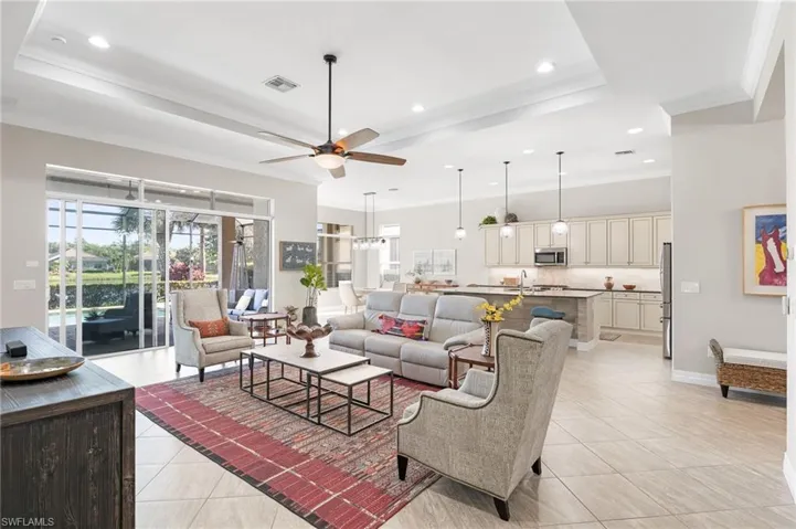 Open-concept main area featuring a tray ceiling with recessed lighting, large-format tile flooring, kitchen island with stone countertop, and sliding glass doors