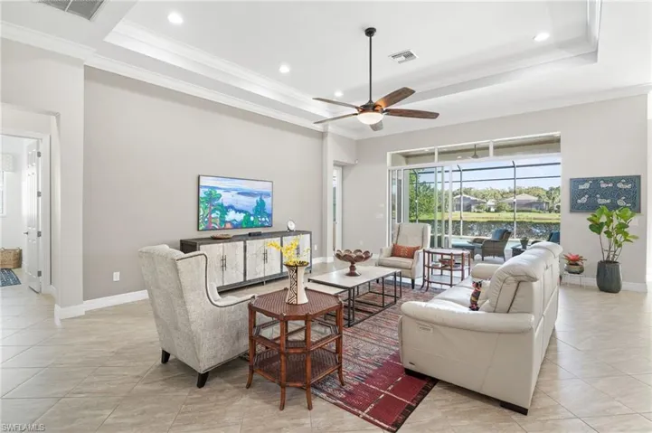 Tray ceiling with recessed lighting, tile flooring, ceiling fan, and large multi-panel sliding glass doors opening to a screened-in lanai