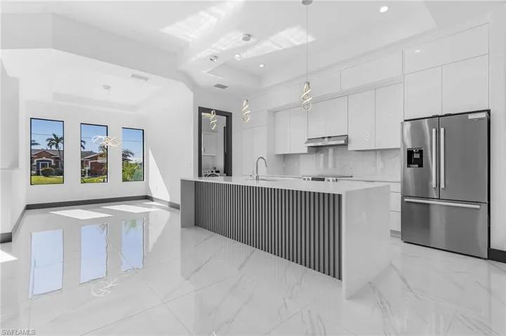 Kitchen featuring white cabinetry, stainless steel refrigerator with ice dispenser, an island with sink, pendant lighting, and a tray ceiling