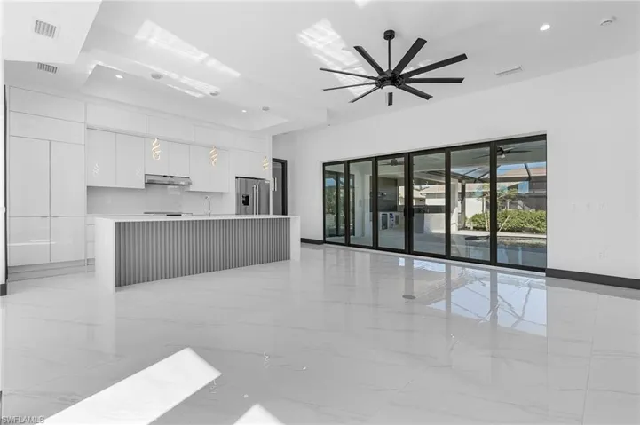 Kitchen featuring white cabinetry, sink, ceiling fan, stainless steel refrigerator with ice dispenser, and an island with sink