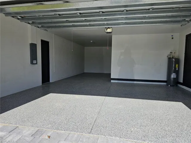 Garage featuring electric panel, electric water heater, and a garage door opener