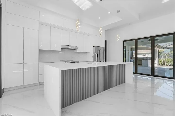 Kitchen featuring white cabinetry, backsplash, decorative light fixtures, high end fridge, and a center island with sink