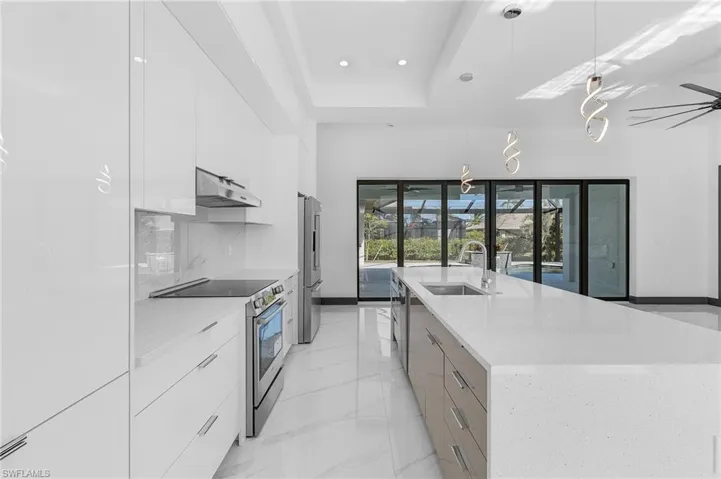 Kitchen with white cabinets, a spacious island, sink, decorative light fixtures, and stainless steel appliances