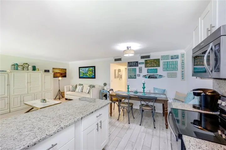 Kitchen with white cabinets, electric range, light stone counters, stainless steel microwave, and crown molding