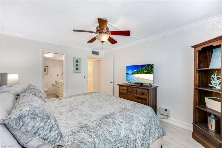 Bedroom with light wood-type flooring, crown molding, ceiling fan, and ensuite bath