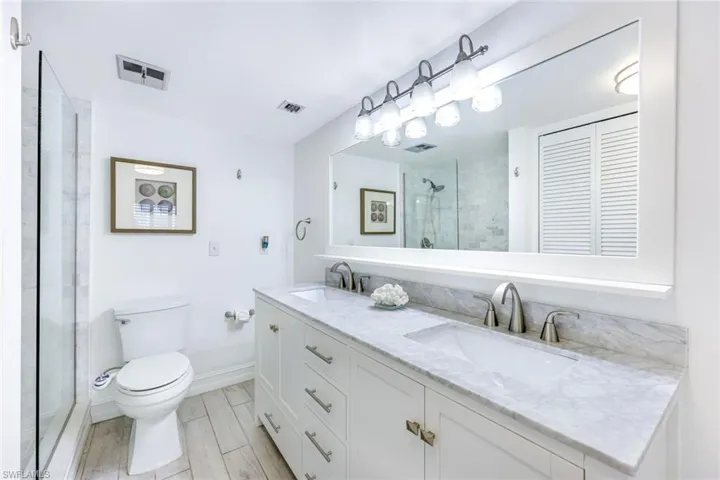 Bathroom with double vanity, a stall shower, wood finish floors, and a closet