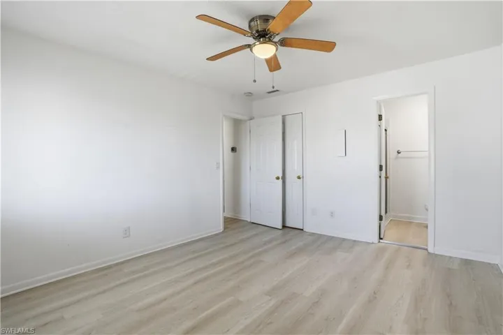 Unfurnished bedroom with light wood-style floors, ceiling fan, and ensuite bathroom