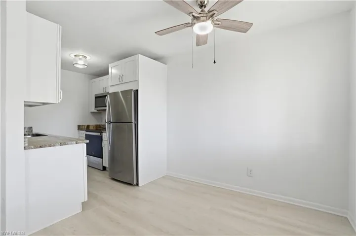 Kitchen featuring stainless steel appliances, white cabinetry, light wood-type flooring, a ceiling fan, and light stone counters