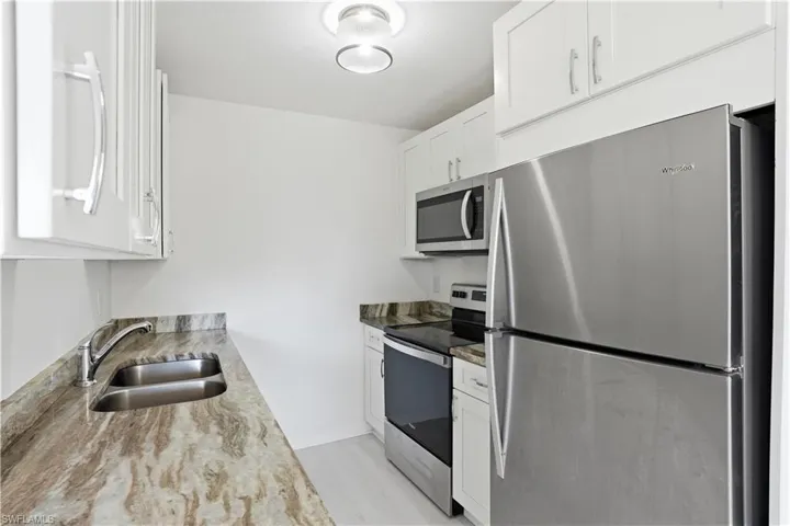 Kitchen featuring stainless steel appliances, white cabinetry, light wood finished floors, and light stone countertops