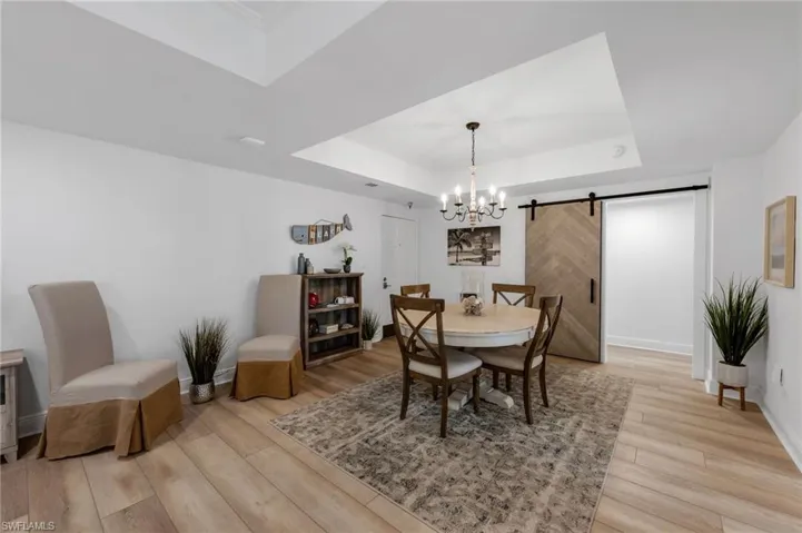 Dining Space Featuring a Barn Door to Primary Bedroom, Tray ceiling, Light Wood-Style LVP Flooring, and a Chandelier