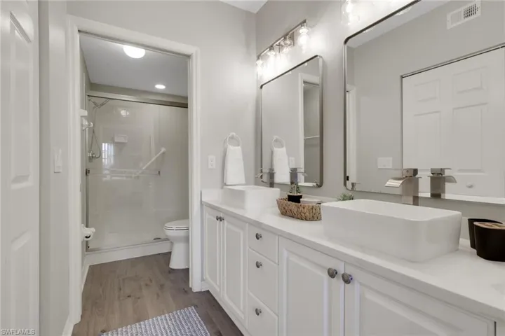 Full bathroom with double vanity, a stall shower, and dark wood-type flooring
