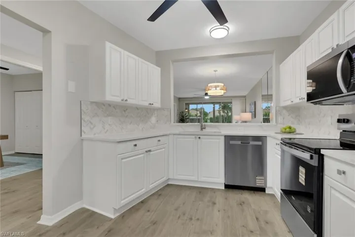 Kitchen with stainless steel appliances, a ceiling fan, white cabinets, light wood finished floors, and backsplash