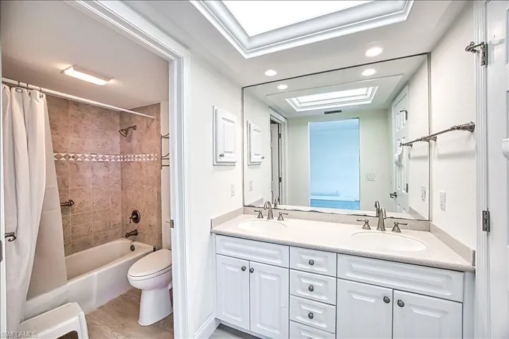 Full bathroom featuring double vanity, toilet, shower / tub combo with curtain, and a sink