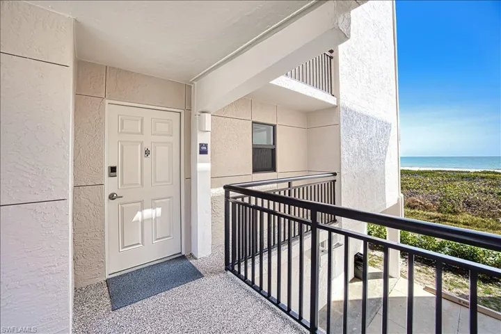 Entrance to property featuring a balcony, a water view, stucco siding, and a beach view