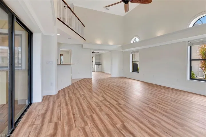 Unfurnished living room with a high ceiling, crown molding, ceiling fan, and light hardwood / wood-style flooring
