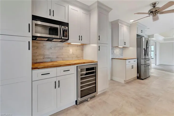 Kitchen with butcher block countertops, appliances with stainless steel finishes, white cabinets, decorative backsplash, and beverage cooler