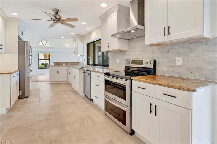 Kitchen featuring wall chimney range hood, appliances with stainless steel finishes, white cabinetry, light stone counters, and decorative backsplash