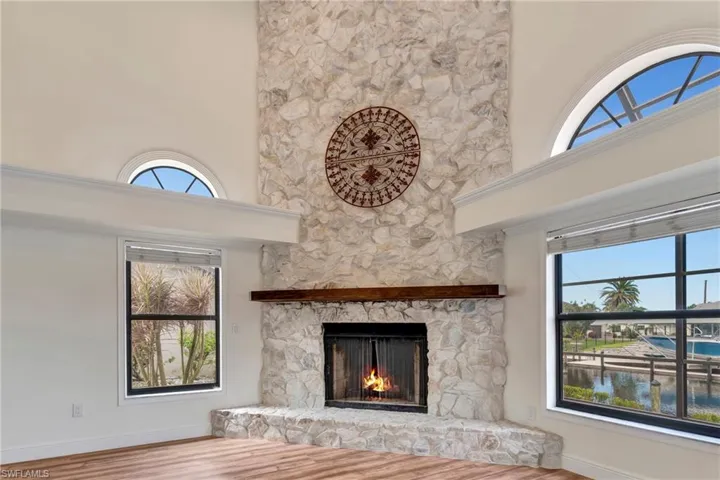 Living room with a water view, wood-type flooring, a stone fireplace, and towering ceiling