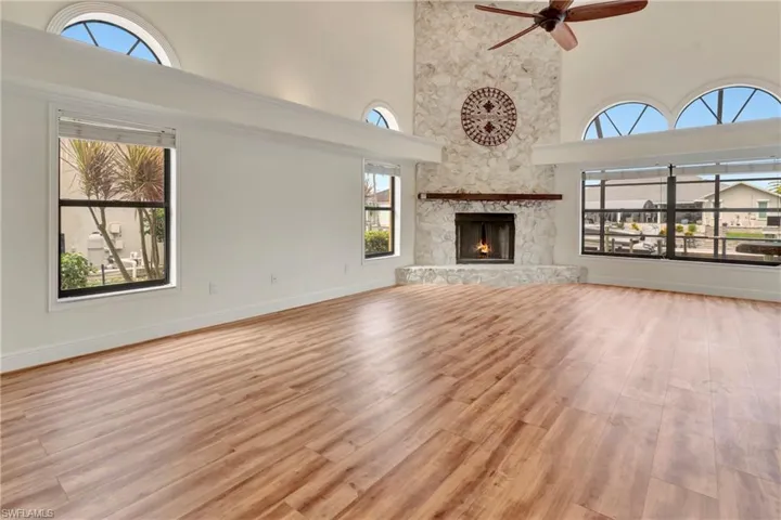 Unfurnished living room featuring a stone fireplace, a towering ceiling, ceiling fan, and light hardwood / wood-style floors