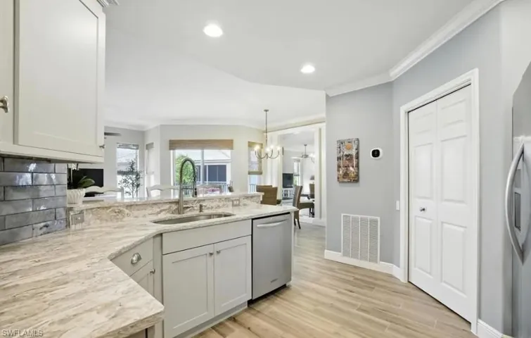 Kitchen featuring crown molding, a peninsula, appliances with stainless steel finishes, light wood finished floors, and pendant lighting