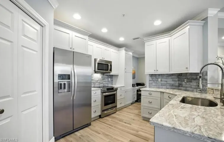 Kitchen featuring stainless steel appliances, light stone counters, crown molding, light wood-style floors, and white cabinets
