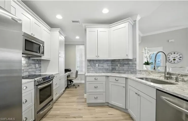 Kitchen featuring appliances with stainless steel finishes, light stone countertops, light wood-type flooring, white cabinets, and recessed lighting