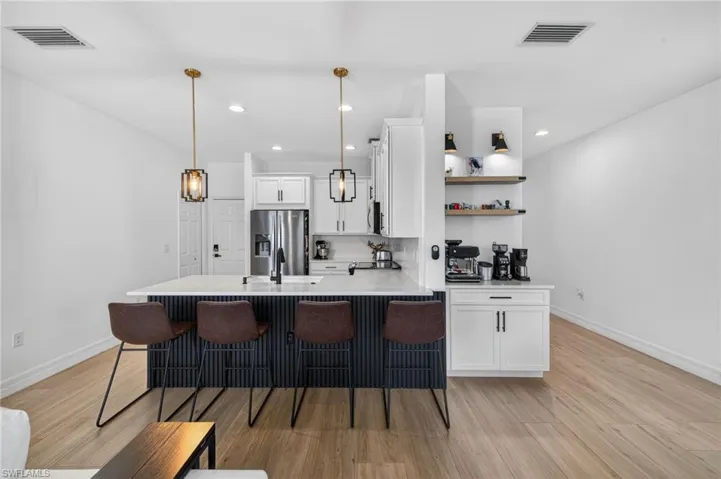 Kitchen with a peninsula, white cabinets, a breakfast bar area, decorative light fixtures, and light wood finished floors